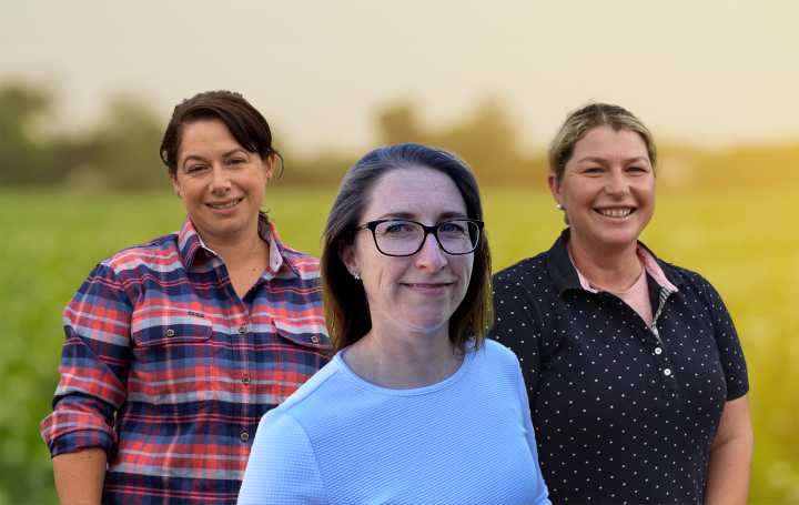 Three smiling women in front of a green field