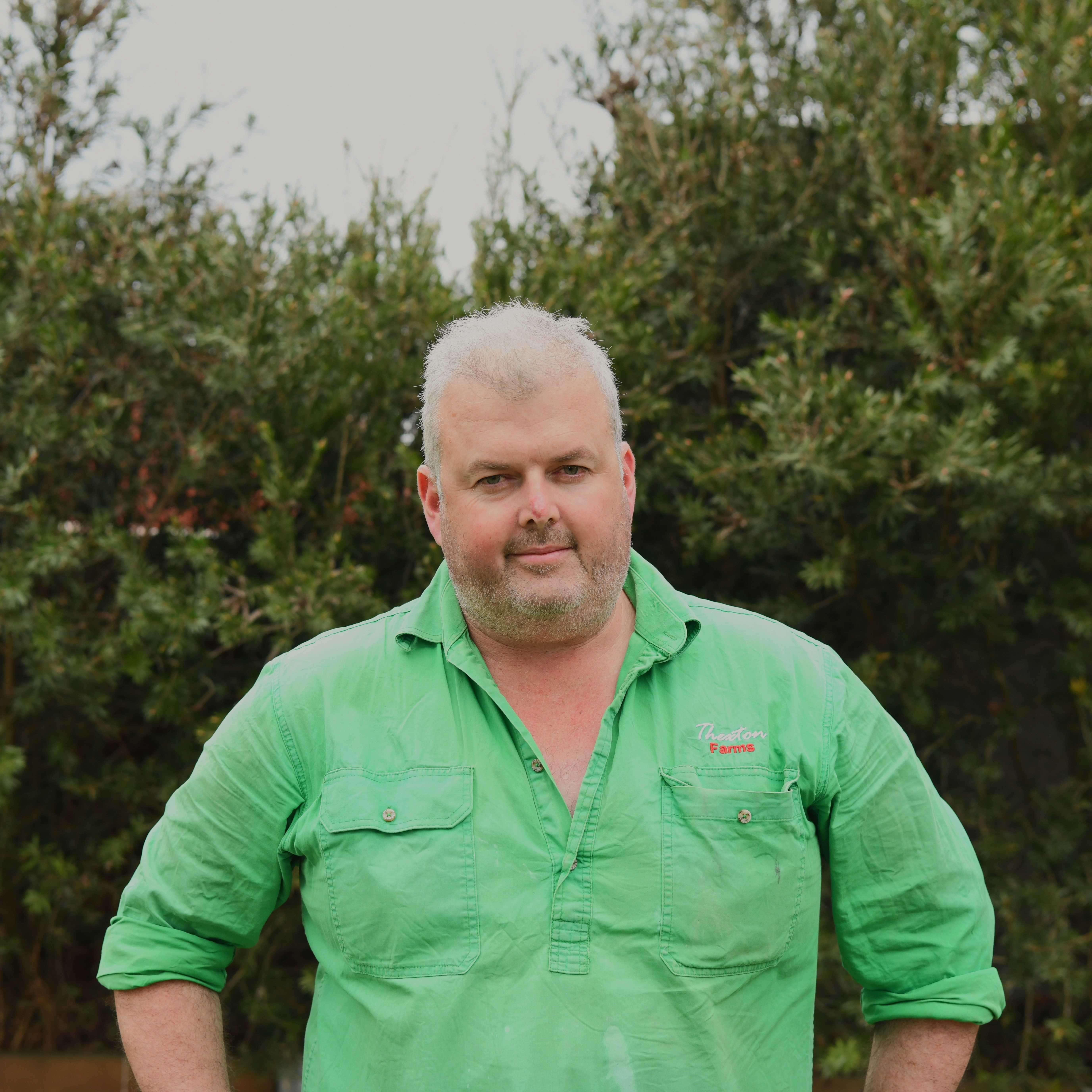 man smiling at the camera wearing a bright green shirt behind a leafy green backdrop.