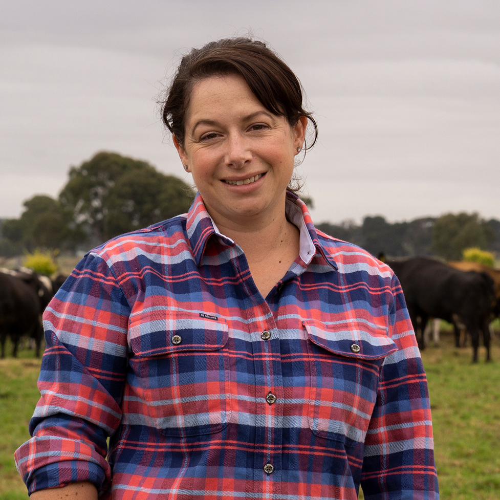 Smiling woman standing in front of cows in a green field with 