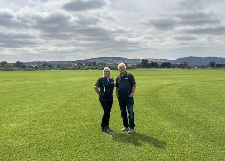 A man and woman standing on a large field of short grass