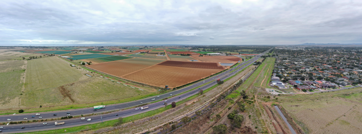 Drone shot of a highway dividing paddocks and a suburban housing area