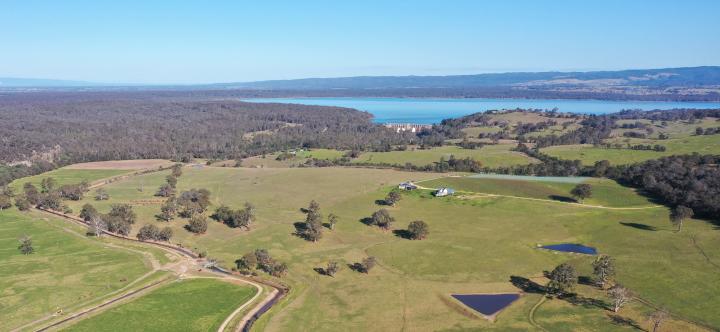 Drone shot of a dam wall with a lake behind it and green paddocks in front