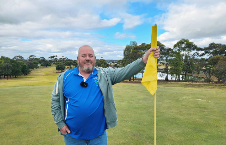 Man holding a yellow golf flag on a green golf course