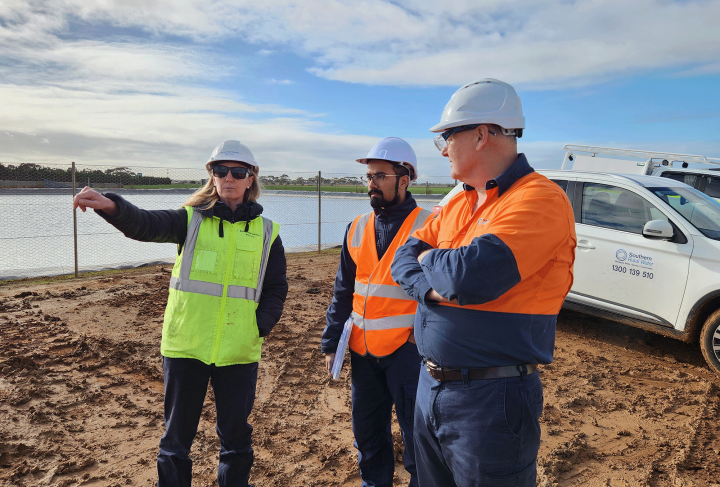 Three people in high vis and hard hats, standing on a project site