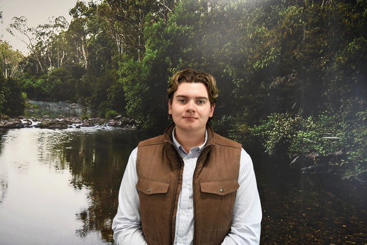 Young man smiling at the camera sitting in front of a green meeting room backdrop