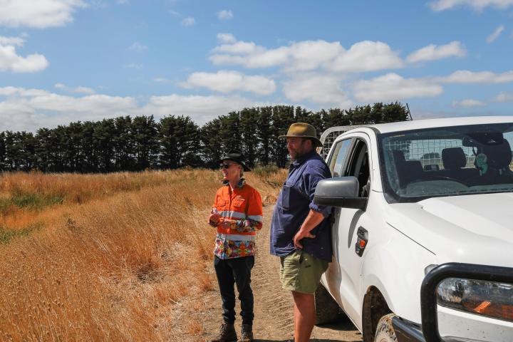 two people standing near a vehicle in a dry paddock