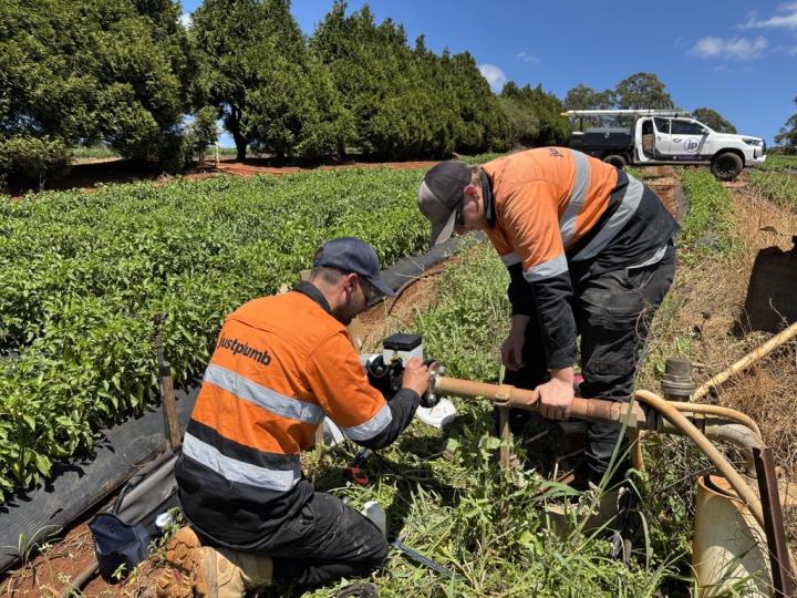 Two men in high visibility jackets working on a meter in a crop field 