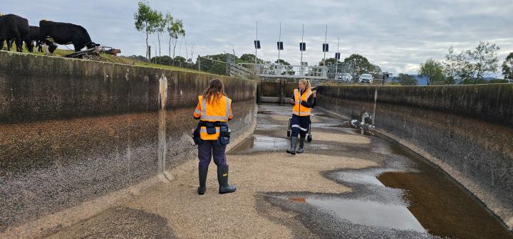 Two women in high visibility vests assess and empty concrete channel