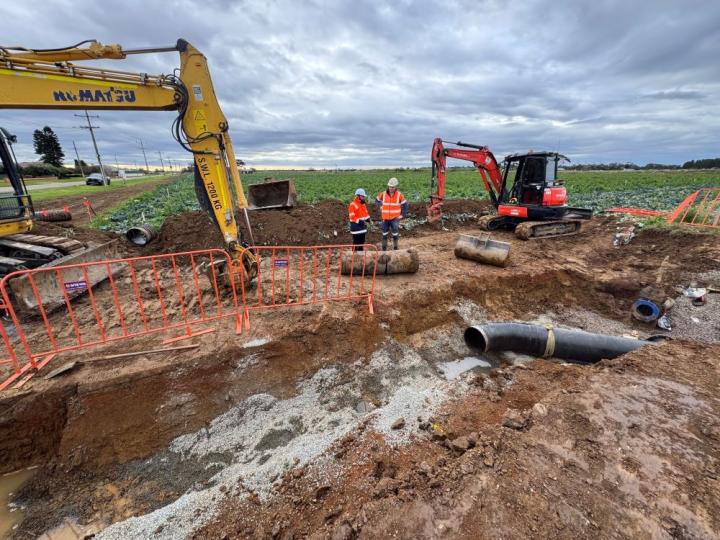 Outdoor works site with two excavators by a dirt trench with pipes sitting in it