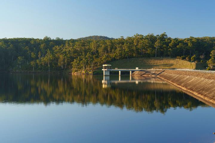 Glassy blue lake with a water tower and dam wall surrounded by green trees 